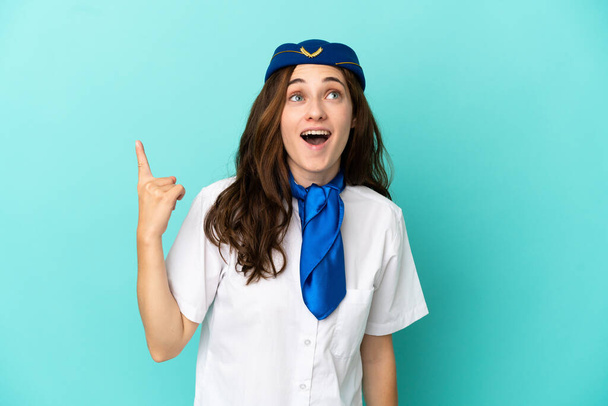 Airplane stewardess woman isolated on blue background pointing up and surprised - Photo, Image