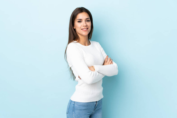Young caucasian woman isolated on blue background with arms crossed and looking forward - Foto, imagen