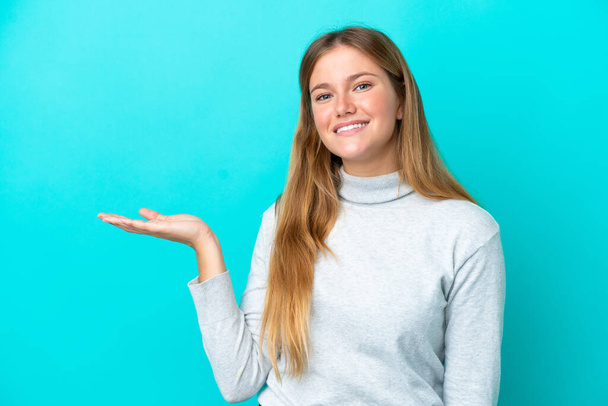 Young blonde woman isolated on blue background holding copyspace imaginary on the palm to insert an ad - Photo, Image