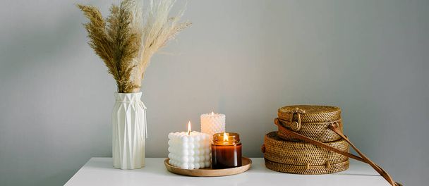 Home interior decor in beige neutral colors. White dresser with dried flowers in vase, rattan bags and candle. Still life, hygge concept - Photo, image