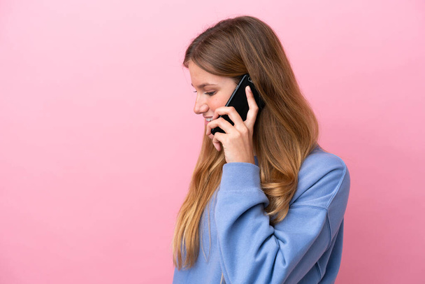 Fiatal szőke nő elszigetelt rózsaszín háttér miközben egy beszélgetést a mobiltelefon valakivel - Fotó, kép