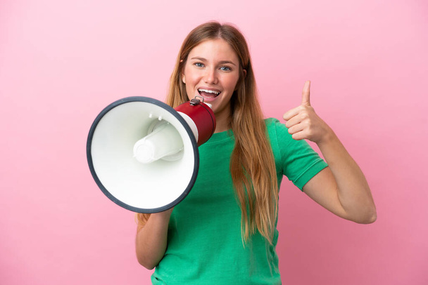 Young blonde woman isolated on pink background shouting through a megaphone and pointing side - Foto, Imagem