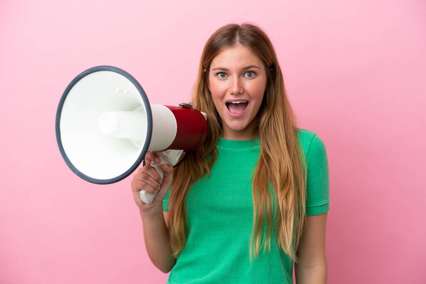 Young blonde woman isolated on pink background holding a megaphone and with surprise expression - Фото, зображення