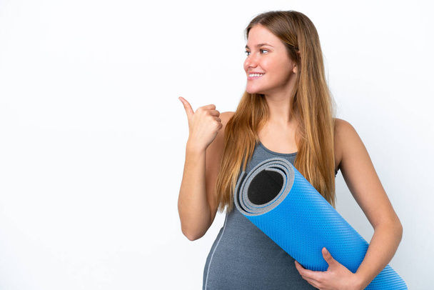 Jeune femme sportive allant à des cours de yoga tout en tenant un tapis pointant vers le côté pour présenter un produit - Photo, image