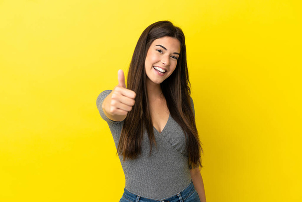 Young Brazilian woman isolated on yellow background with thumbs up because something good has happened - Photo, Image