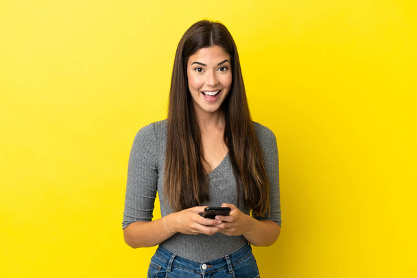 Young Brazilian woman isolated on yellow background surprised and sending a message - Photo, Image