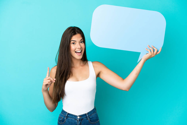 Young Brazilian woman isolated on blue background holding an empty speech bubble with surprised expression - Foto, Bild