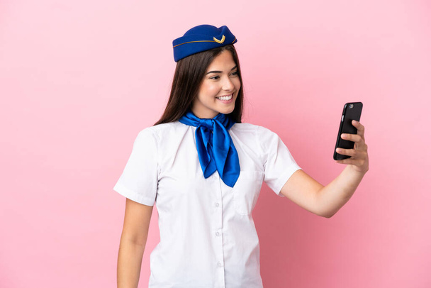 Airplane stewardess Brazilian woman isolated on pink background making a selfie - 写真・画像