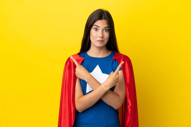 Super Hero Brazilian woman isolated on yellow background pointing to the laterals having doubts - Photo, Image