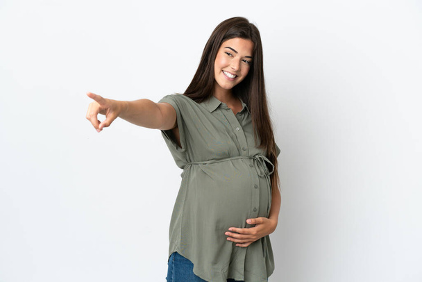 Молода бразилька, ізольована на білому тлі, вагітна і вказує на передній план. - Фото, зображення