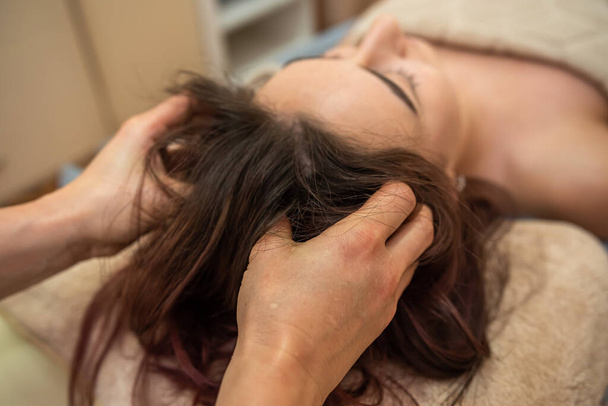 beautiful young girl with dark hair doing a head massage in a massage parlor. Head massage concept - 写真・画像