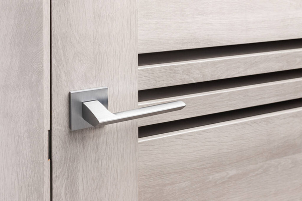 Close up of stylish metal door knob on modern interior door. Silver chrome door handle on light beige door with three strips of frosted glass. Concept of interior details. - Photo, Image