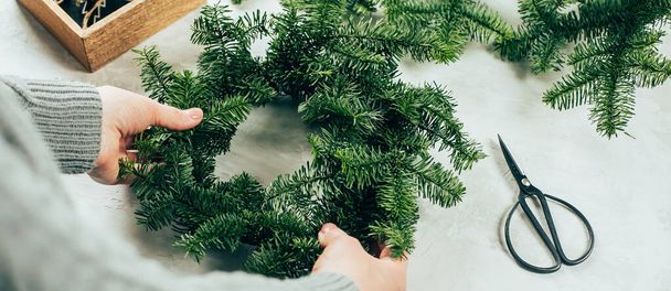 Woman making a christmas fir wreath. Christmas decorating for home interior. Long banner image for design - Photo, Image
