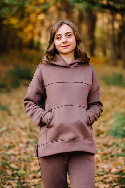 Young woman in hoodie sweater smiling in an autumn park. Sunny weather. Fall season. - Fotó, kép