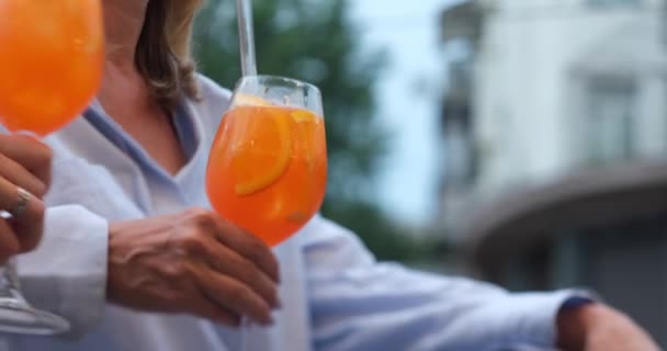 Friends hanging out in a bar clinking with glasses of Spritz cocktail. Aperol spritz cocktail, close up shot. Refreshing alcoholic drink in the hands. No faces. High quality 4k footage - Materiał filmowy, wideo