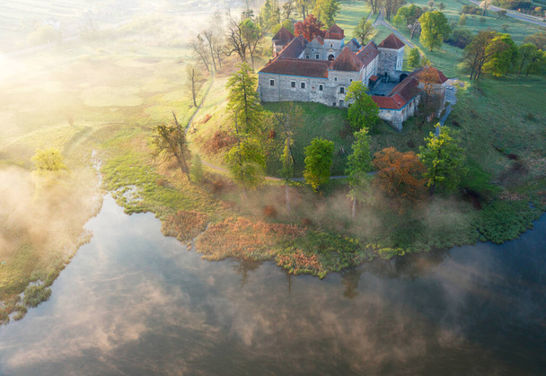 Letecký pohled na hrad Svirzh u Lvova, Ukrajina v ranní mlze za úsvitu. Jezero a okolní krajina při východu slunce. - Fotografie, Obrázek