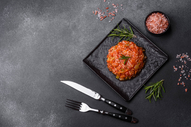 Boiled rice with peppers, spices, herbs and tomato sauce on a black slate plate on a grey concrete background - 写真・画像