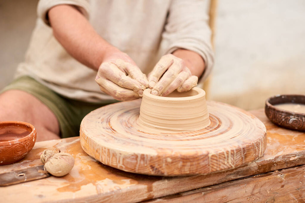 male craftsman master in light linen shirt sculpts jug, bowl or vase from clay in village - Foto, Imagem