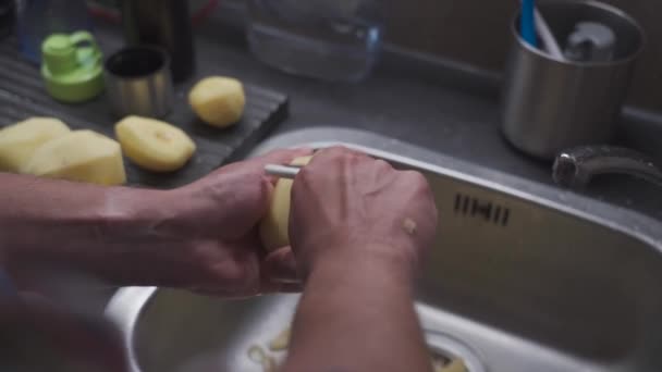 Husband peels potatoes with a tool for cleaning vegetables and making dinner. Health food topic, man peeling raw potato with a knife over kitchen sink. Organic, greenhouse vegetables from the farm.  - Záběry, video