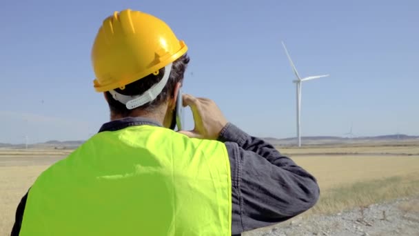 Anonymous man in uniform calls on the phone during inspection on wind farm in summer. Vertical video 4K - Video