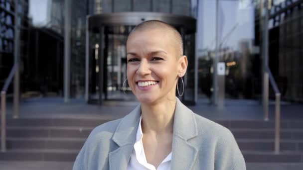 Cheerful middle-aged empowered woman with shaved hair looking at camera. Business people outdoors on background with buildings. corporate. High quality photo - Video