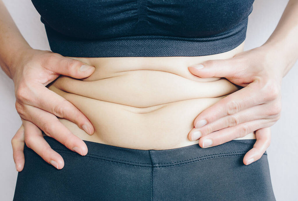 Close-up of Woman touching her fat belly, woman's hand holding excessive belly fat. Being overweight is one of the leading causes of major diseases such as heart disease, stroke, high blood pressure. - Photo, image