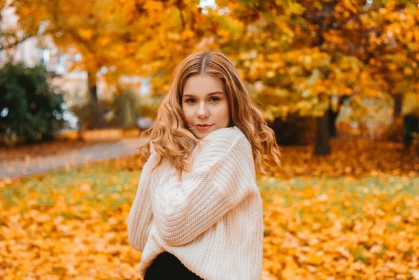 Photo portrait of a girl in a white sweater, beautiful brunette . Pretty woman in the park in autumn  Autumn fashion and style - Photo, Image