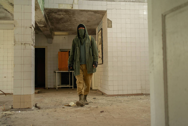 Un joven caminando en un edificio abandonado. vagabundo. hombre con una capa protectora con una capucha. Post apocalipsis. Viajar a pie en un mundo post-apocalíptico. - Foto, Imagen