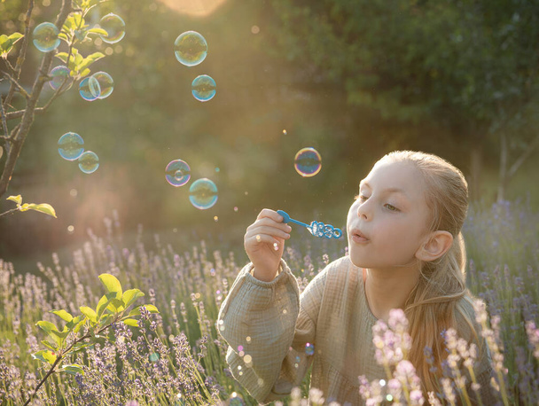 Beautiful little girl blowing soap bubbles in a field with lavender  - Fotó, kép