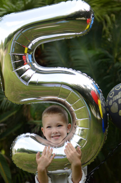 Poika juhlii syntymäpäiväänsä. Viisi vuotta. Lapsi, jolla on ilmapalloja puistossa. Lasten loma, lahjat, hyvä tunnelma.  - Valokuva, kuva