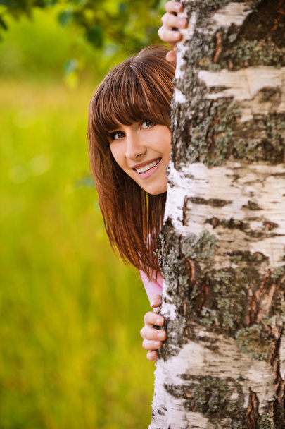 Porträt eines lachenden Mädchens, das von einem Baum aus blickt - Foto, Bild