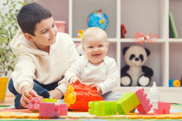 happy older brother plays with sister with colourful building blocks at home or kindergarten - Φωτογραφία, εικόνα