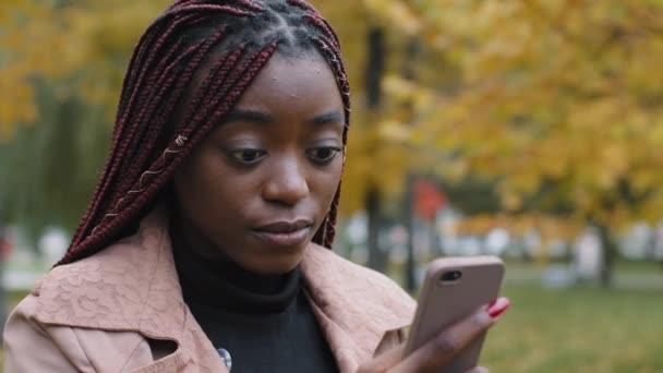 Close-up young puzzled pensive woman looking at phone screen receiving incomprehensible message focused girl writes sms communicates on Internet using smartphone checking email on telephone outdoors - Filmagem, Vídeo