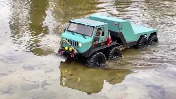 RC flatbed towing truck moving in shallow water in slow motion. Radio controlled vehicle in a pond. - Video