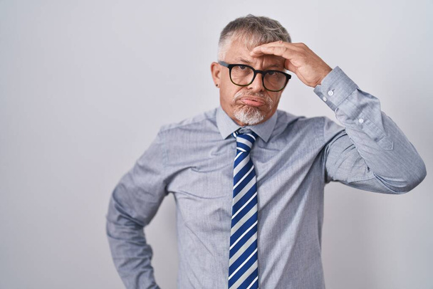 Hombre de negocios hispano con cabello gris que lleva gafas preocupado y estresado por un problema con la mano en la frente, nervioso y ansioso por la crisis  - Foto, imagen