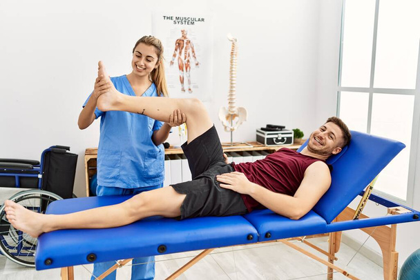 Mujer fisioterapeuta hispana joven hace tratamiento de rehabilitación de piernas al hombre en la clínica. - Foto, imagen