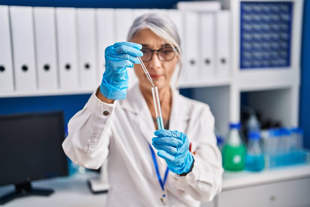 Жінка середнього віку сіро-волохата вчена наливає рідину на пробірку в лабораторії
 - Фото, зображення