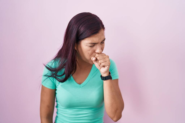 ピンクの背景に立つ若いヒスパニック系の女性は気分が悪く、風邪や気管支炎の症状として咳をします。ヘルスケアの概念.  - 写真・画像
