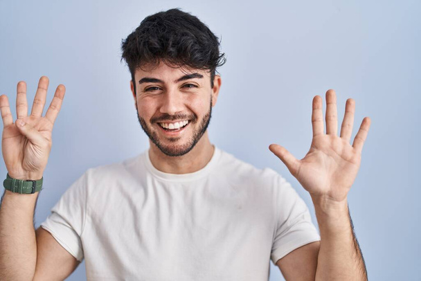 Hispanic man with beard standing over white background showing and pointing up with fingers number nine while smiling confident and happy.  - Fotó, kép