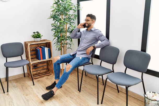 Nuori arabi mies puhuu älypuhelimeen istuu tuolilla odotushuoneessa - Valokuva, kuva