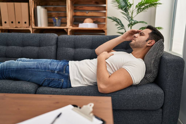 Jovem hispânico estressado tendo terapia mental deitado no sofá no centro de psicologia - Foto, Imagem
