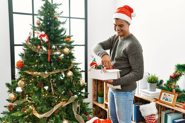 Genç İspanyol adam gülümsüyor. Evde kendine güvenen bir Noel ağacı süslüyordu. - Fotoğraf, Görsel