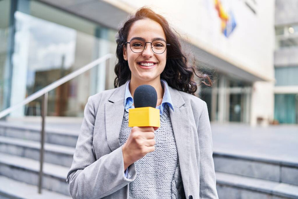 Jovem mulher hispânica repórter trabalhando usando microfone na rua - Foto, Imagem
