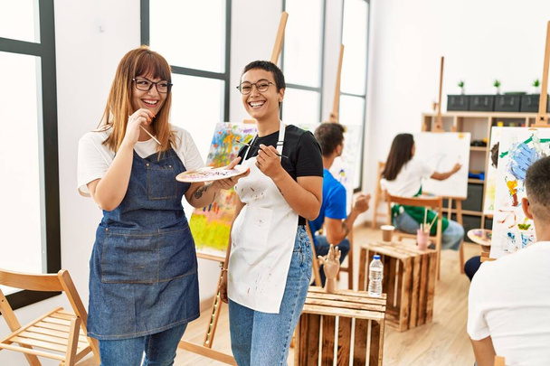 Две женщины улыбаются счастливым рисунком с группой людей в художественной студии. - Фото, изображение