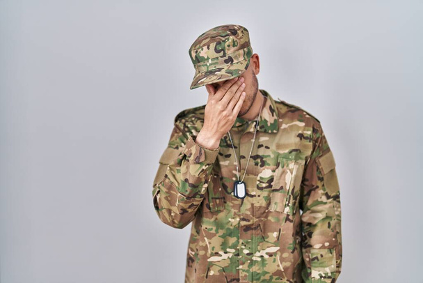 Молодой латиноамериканец в камуфляжной армейской униформе устал тереть нос и глаза, чувствуя усталость и головную боль. концепция стресса и разочарования.  - Фото, изображение