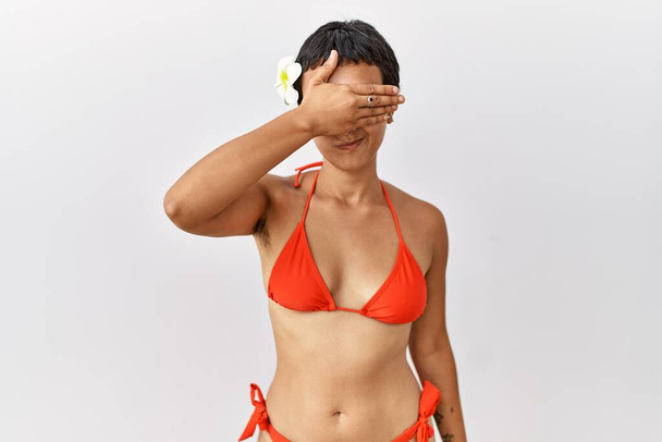 Jonge Latijns-Amerikaanse vrouw met kort haar in bikini die ogen met de hand bedekt en er ernstig en verdrietig uitziet. gezichtsloosheid, verstoppertje en afwijzing  - Foto, afbeelding