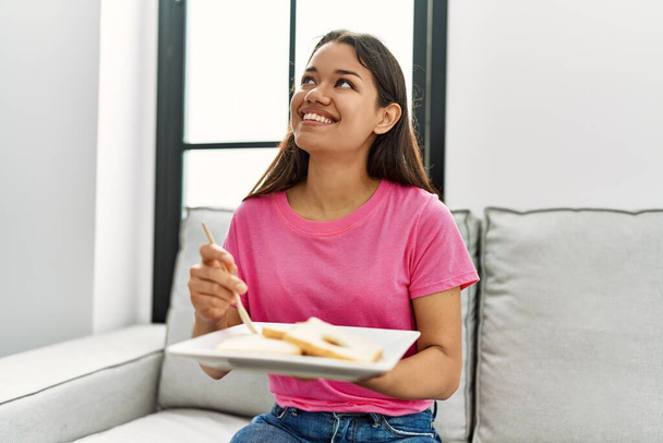 若いですラテン女性持っている昼食を持っていますソファに自宅で - 写真・画像
