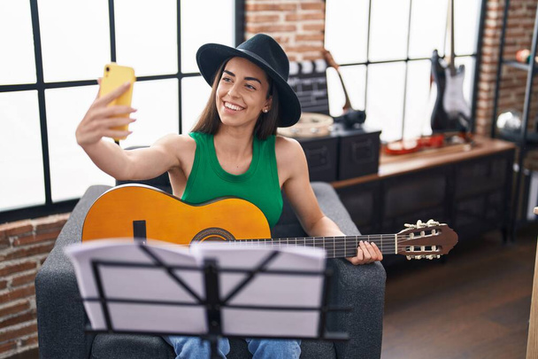 Νεαρή Ισπανίδα μουσικός κάνει selfie από το smartphone παίζει κλασική κιθάρα στο στούντιο μουσικής - Φωτογραφία, εικόνα