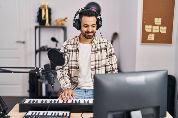 Joven músico hispano cantando canción tocando el teclado del piano en el estudio de música - Foto, imagen