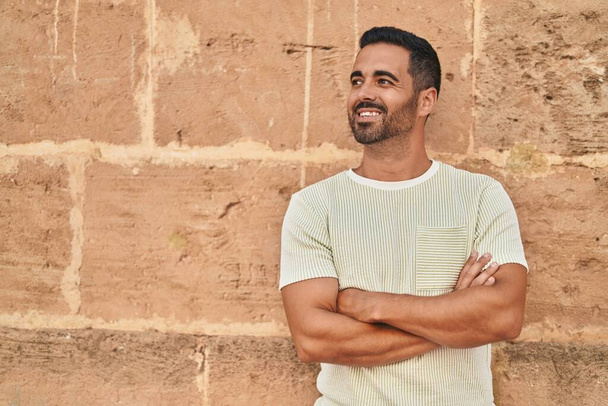 Jeune homme hispanique souriant confiant debout avec les bras croisés geste sur fond de briques isolées - Photo, image